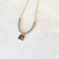 A silver-colored necklace featuring a square freshwater pearl pendant with a cross charm, surrounded by a chain of pearls on a marble surface.
